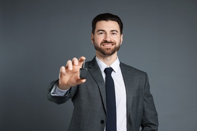 Cheerful salesman with car key on grey background