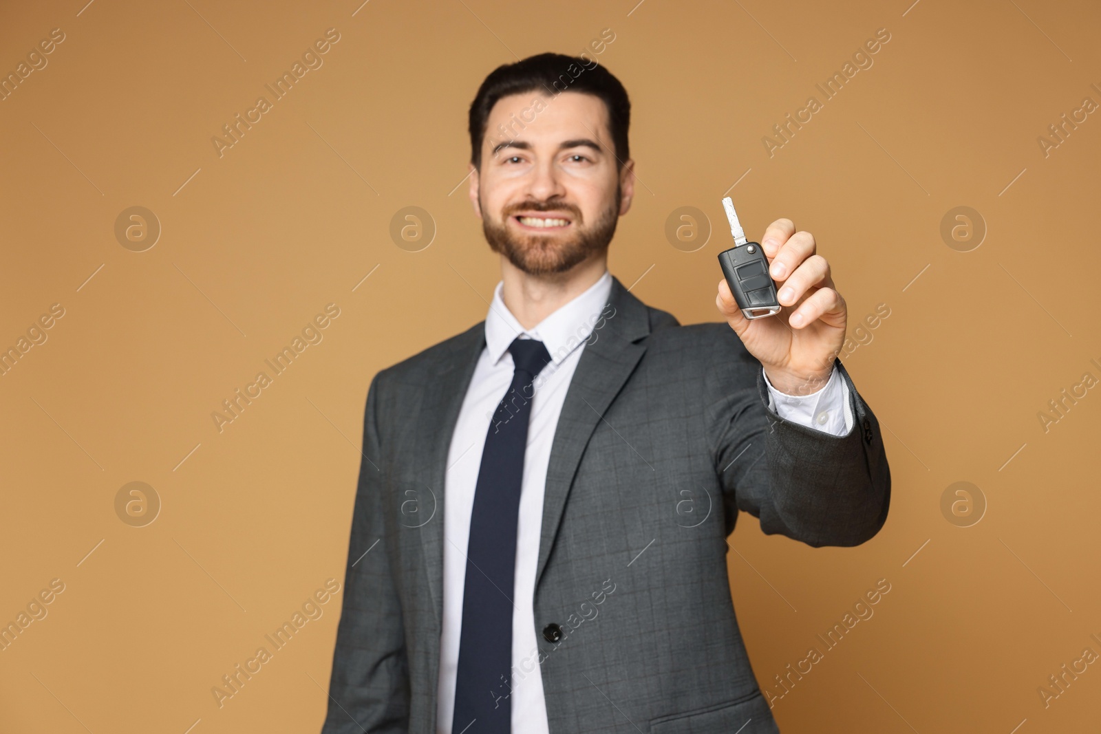 Photo of Cheerful salesman with car key on beige background