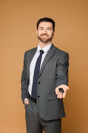 Cheerful salesman with car key on beige background