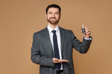 Photo of Cheerful salesman showing car key on beige background