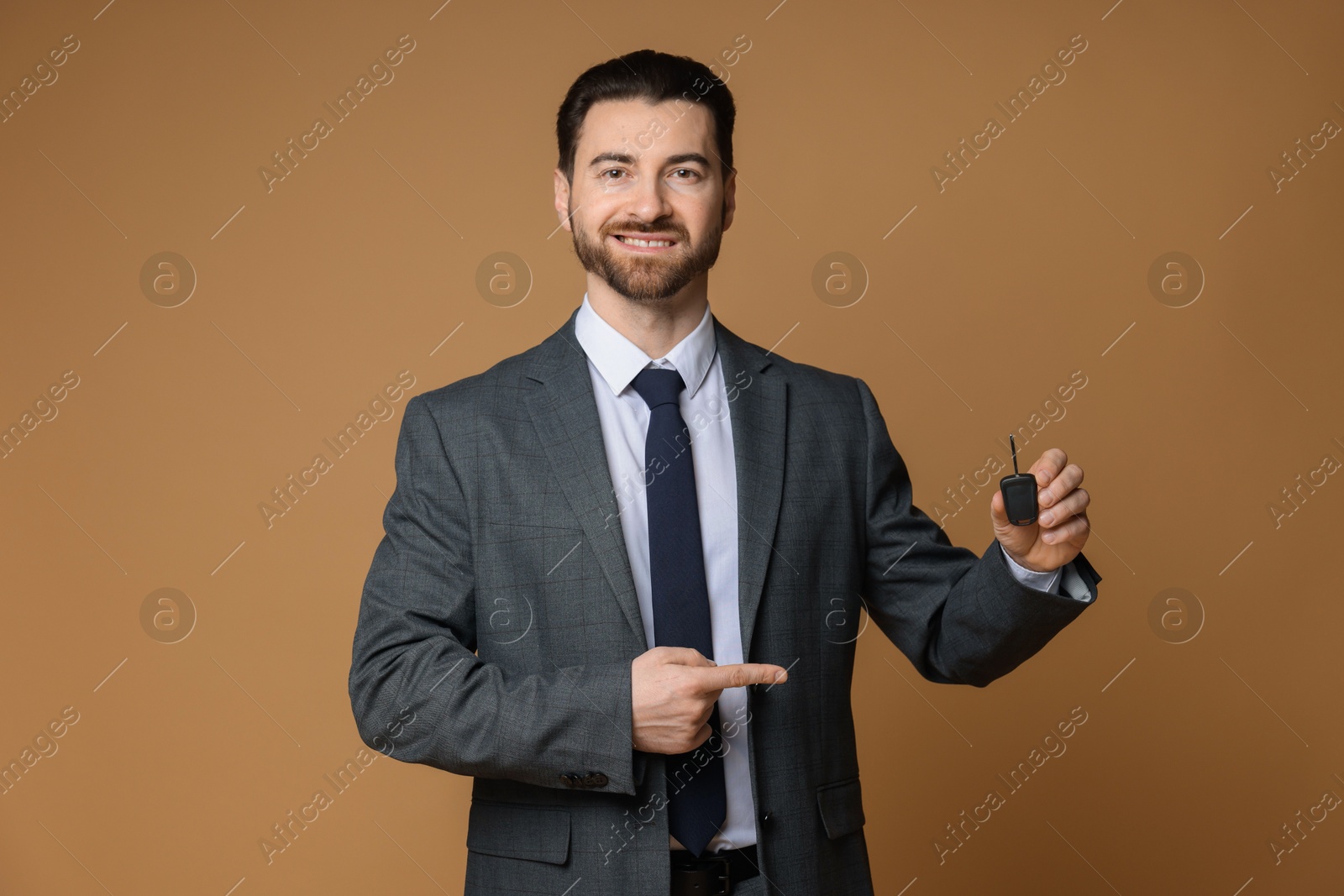 Photo of Cheerful salesman pointing at car key on beige background