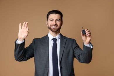 Cheerful salesman with car key showing okay gesture on beige background