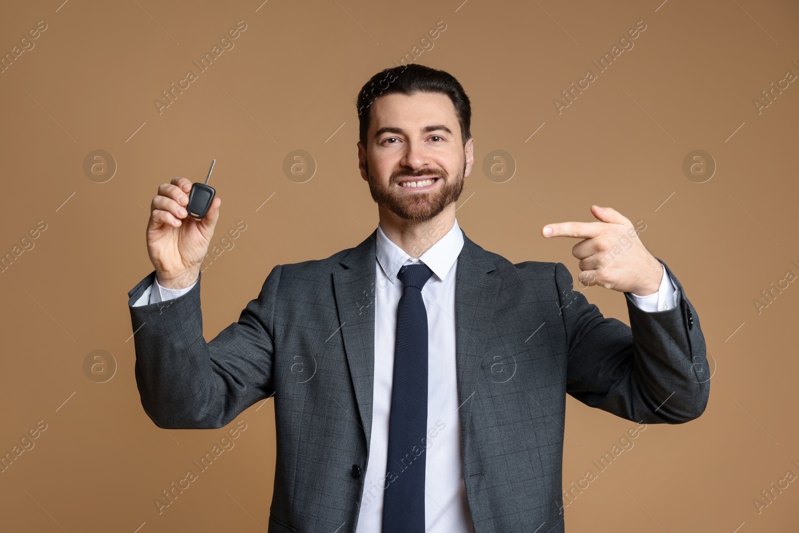 Photo of Cheerful salesman pointing at car key on beige background