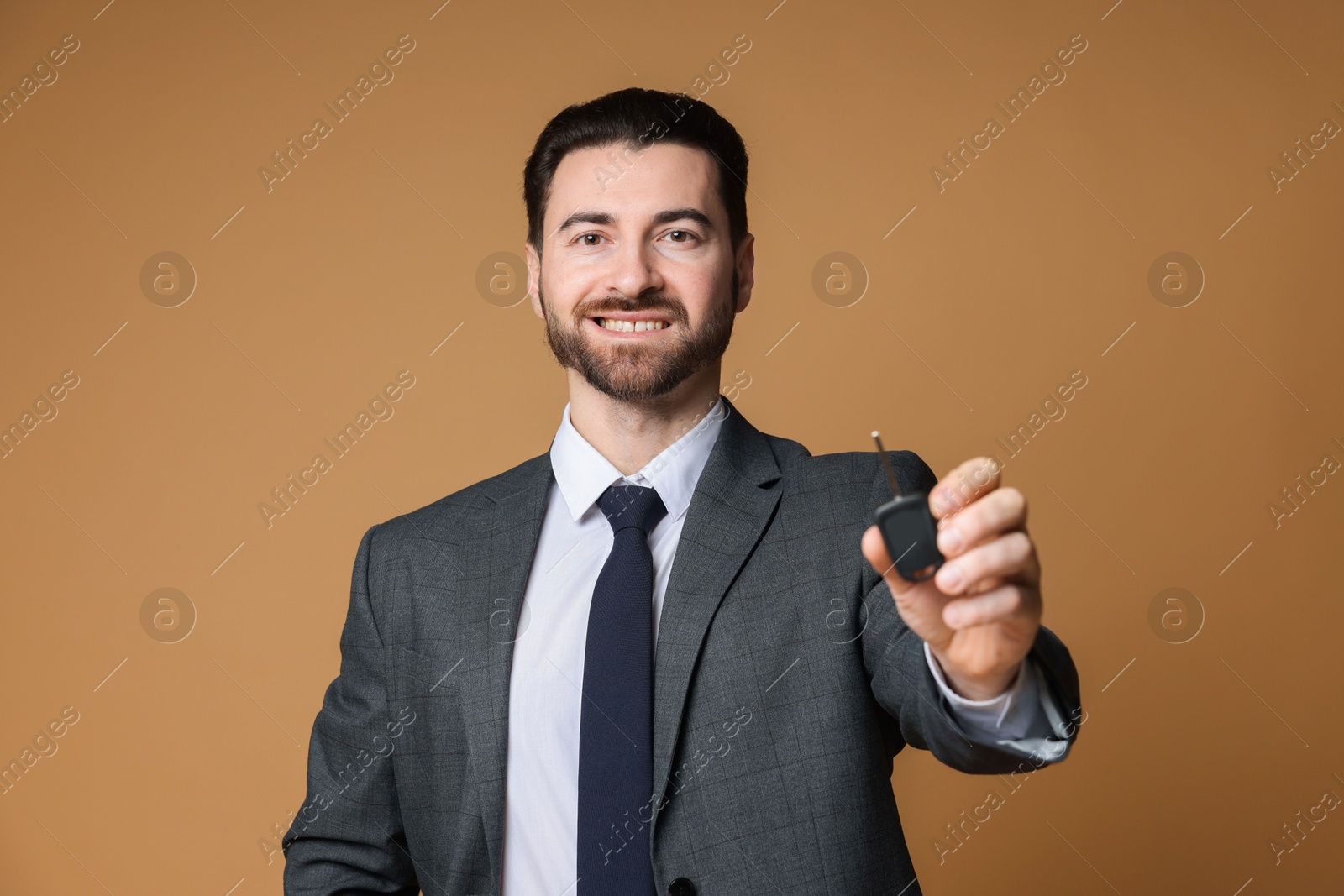 Photo of Cheerful salesman with car key on beige background