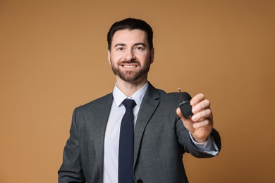 Cheerful salesman with car key on beige background