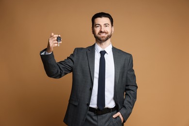 Cheerful salesman with car key on beige background