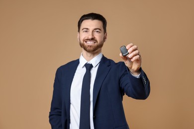 Photo of Cheerful salesman with car key on beige background