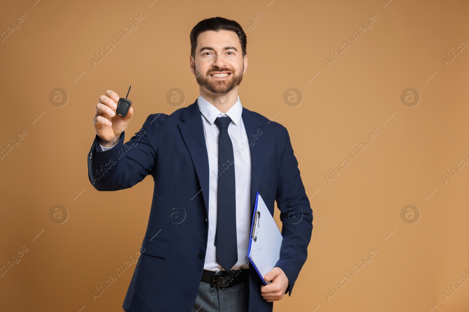 Photo of Cheerful salesman with car key and clipboard on beige background