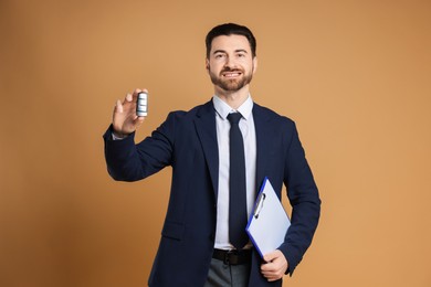 Photo of Cheerful salesman with car key and clipboard on beige background