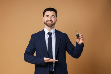 Photo of Cheerful salesman showing car key on beige background