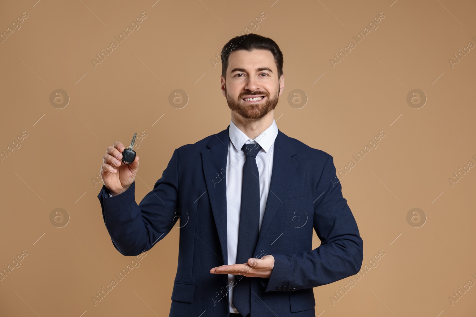 Photo of Cheerful salesman showing car key on beige background