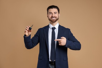 Cheerful salesman pointing at car key on beige background