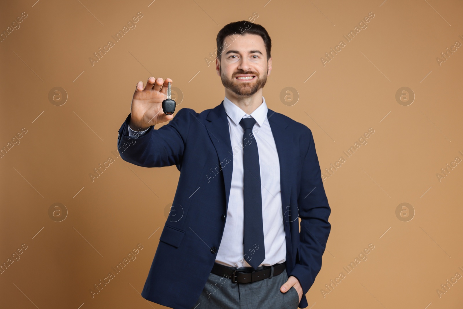 Photo of Cheerful salesman with car key on beige background