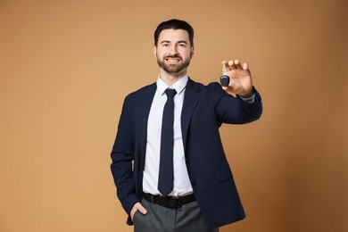 Photo of Cheerful salesman with car key on beige background