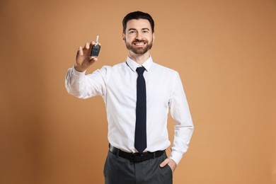 Photo of Cheerful salesman with car key on beige background