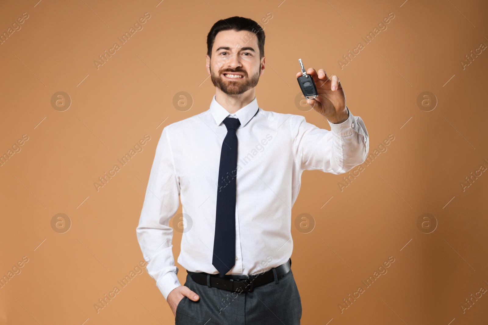 Photo of Cheerful salesman with car key on beige background