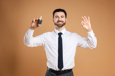 Photo of Cheerful salesman with car key showing okay gesture on beige background