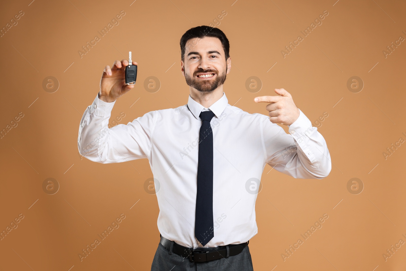 Photo of Cheerful salesman pointing at car key on beige background