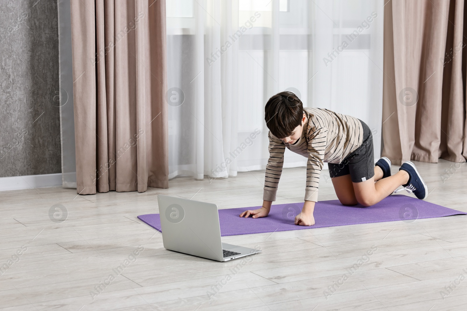 Photo of Little boy exercising near laptop at home. Morning routine