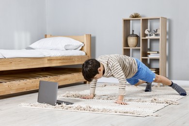 Photo of Little boy exercising near laptop at home. Morning routine