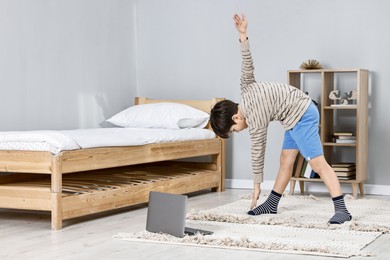 Photo of Little boy exercising near laptop at home. Morning routine