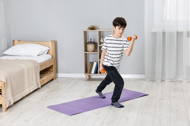 Photo of Little boy exercising with dumbbells at home. Morning routine