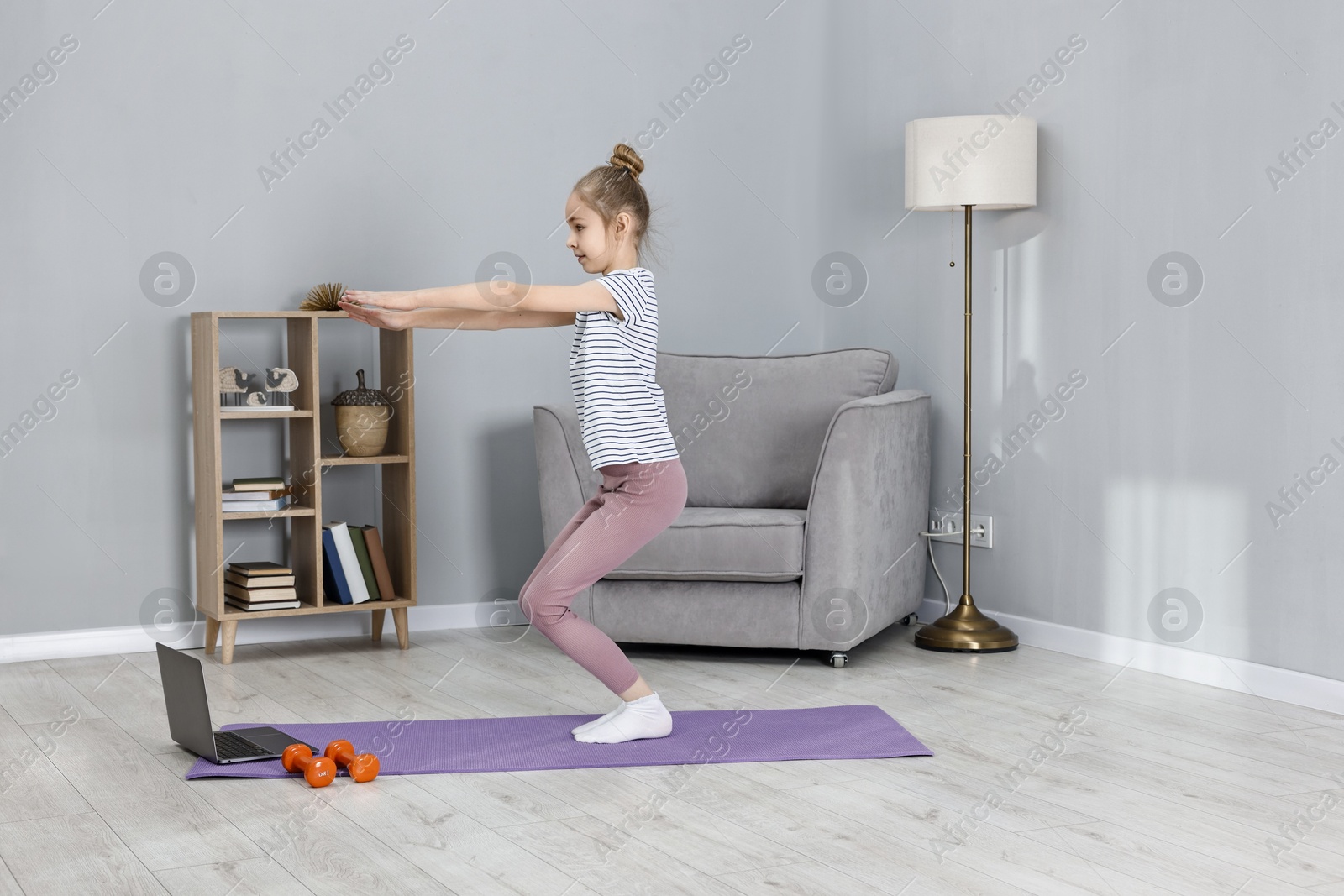 Photo of Little girl exercising near laptop at home. Morning routine