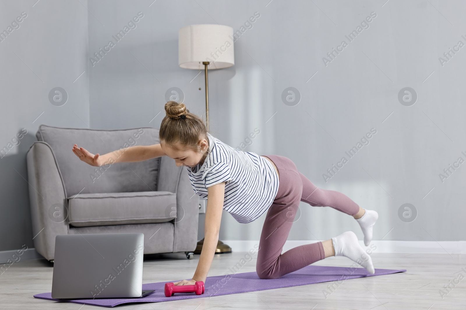 Photo of Little girl exercising near laptop at home, space for text. Morning routine