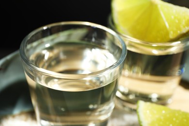 Tequila shots and slices of lime on table against black background, closeup