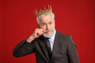 Senior man wearing luxury crown on red background