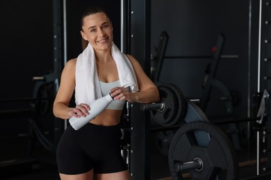 Happy woman with towel and water bottle in gym