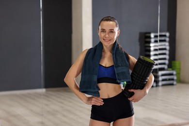 Photo of Happy woman with towel and foam roller in fitness studio