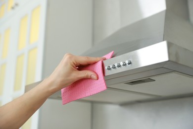 Photo of Woman cleaning kitchen hood with rag indoors, closeup