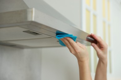 Photo of Woman cleaning kitchen hood with rag indoors, closeup