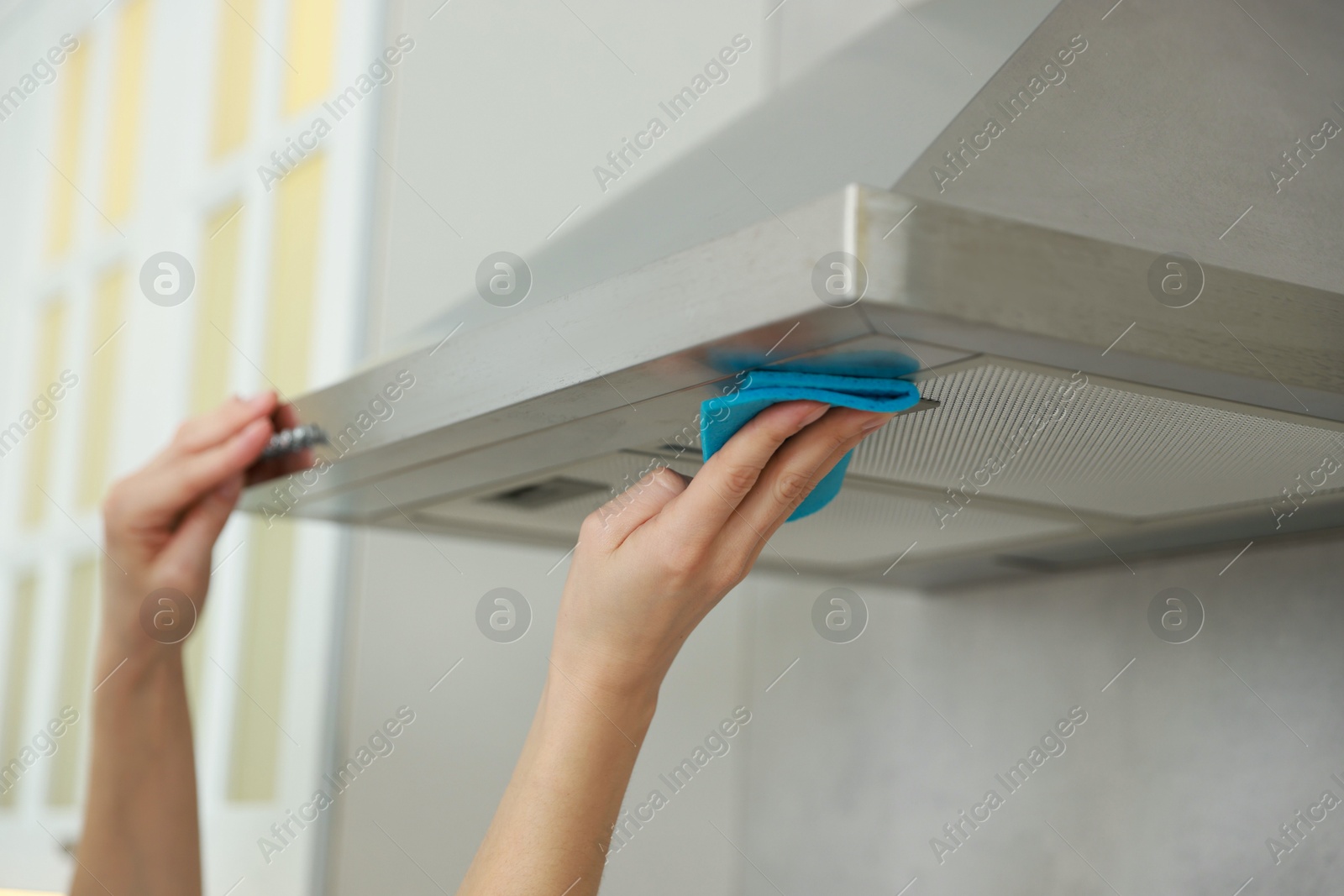 Photo of Woman cleaning kitchen hood with rag indoors, closeup