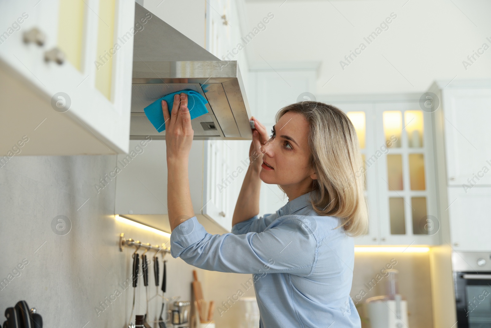 Photo of Woman cleaning kitchen hood with rag indoors