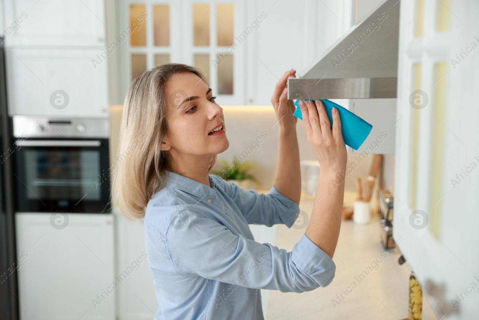 Photo of Woman cleaning kitchen hood with rag indoors