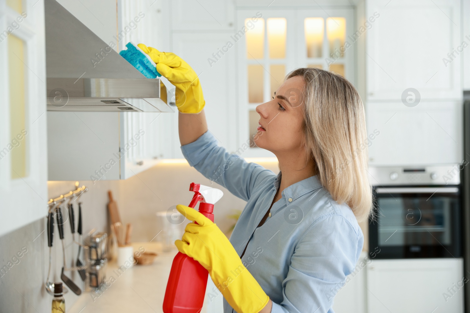 Photo of Woman cleaning kitchen hood with sponge and detergent indoors