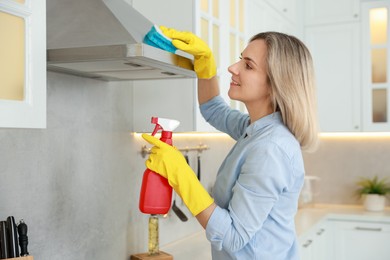 Woman cleaning kitchen hood with sponge and detergent indoors