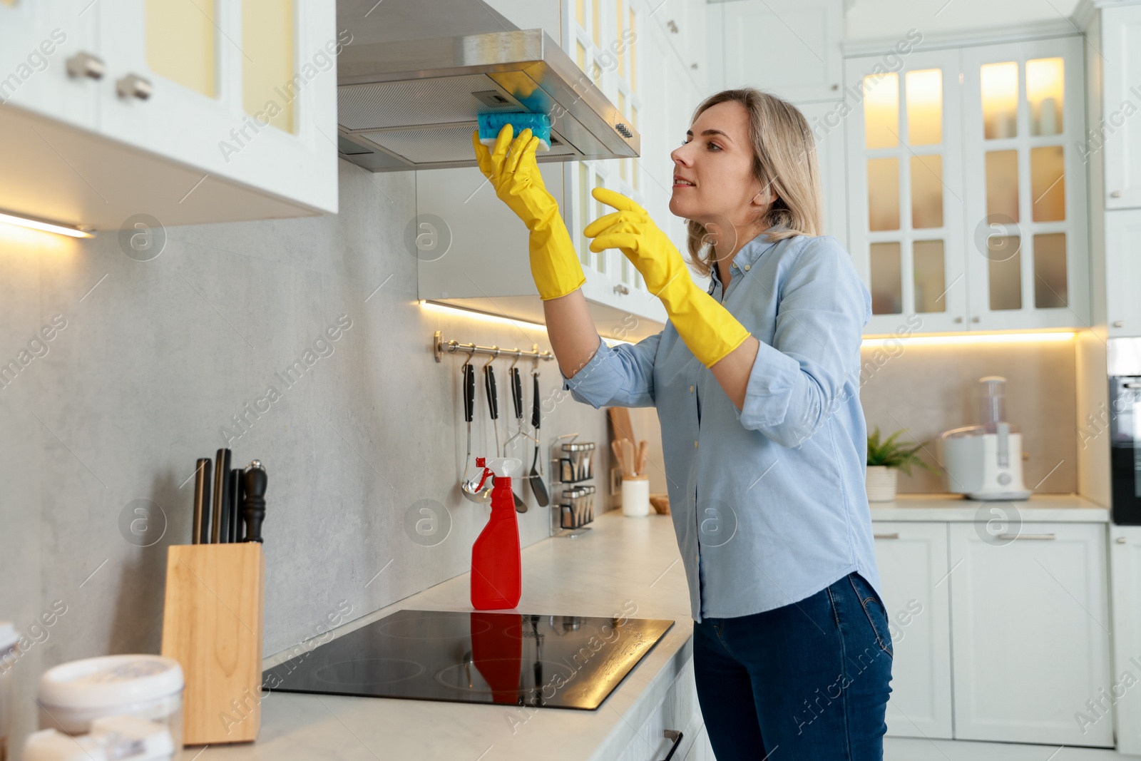 Photo of Woman cleaning kitchen hood with sponge indoors