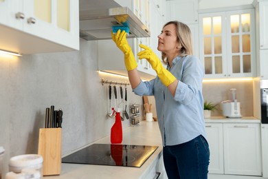 Photo of Woman cleaning kitchen hood with sponge indoors