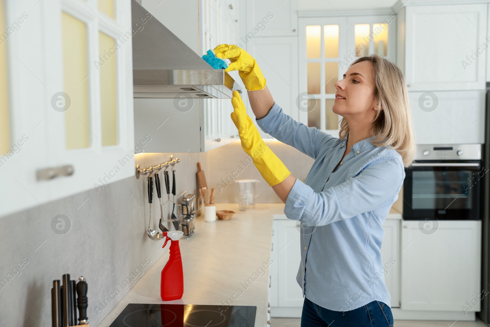 Photo of Woman cleaning kitchen hood with sponge indoors