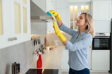 Woman cleaning kitchen hood with sponge indoors