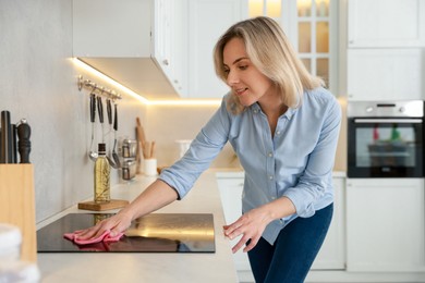 Photo of Woman cleaning induction cooktop with rag indoors