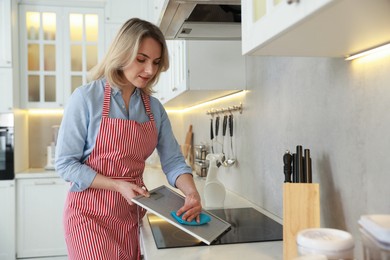 Photo of Woman cleaning filter of kitchen hood with rag indoors