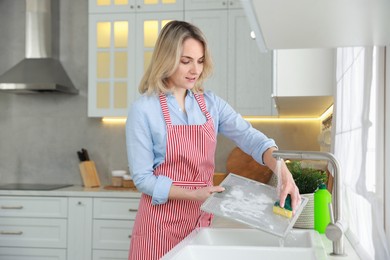 Woman cleaning filter of kitchen hood with sponge above sink indoors