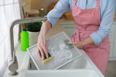 Photo of Woman cleaning filter of kitchen hood with sponge above sink indoors, closeup