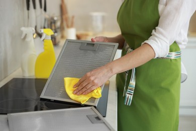 Photo of Woman cleaning filter of kitchen hood with rag indoors, closeup