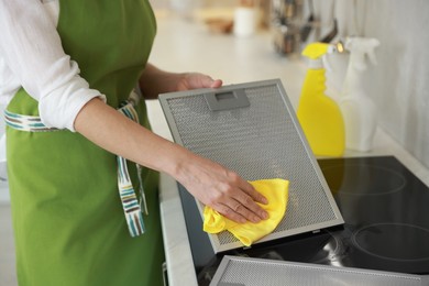 Woman cleaning filter of kitchen hood with rag indoors, closeup