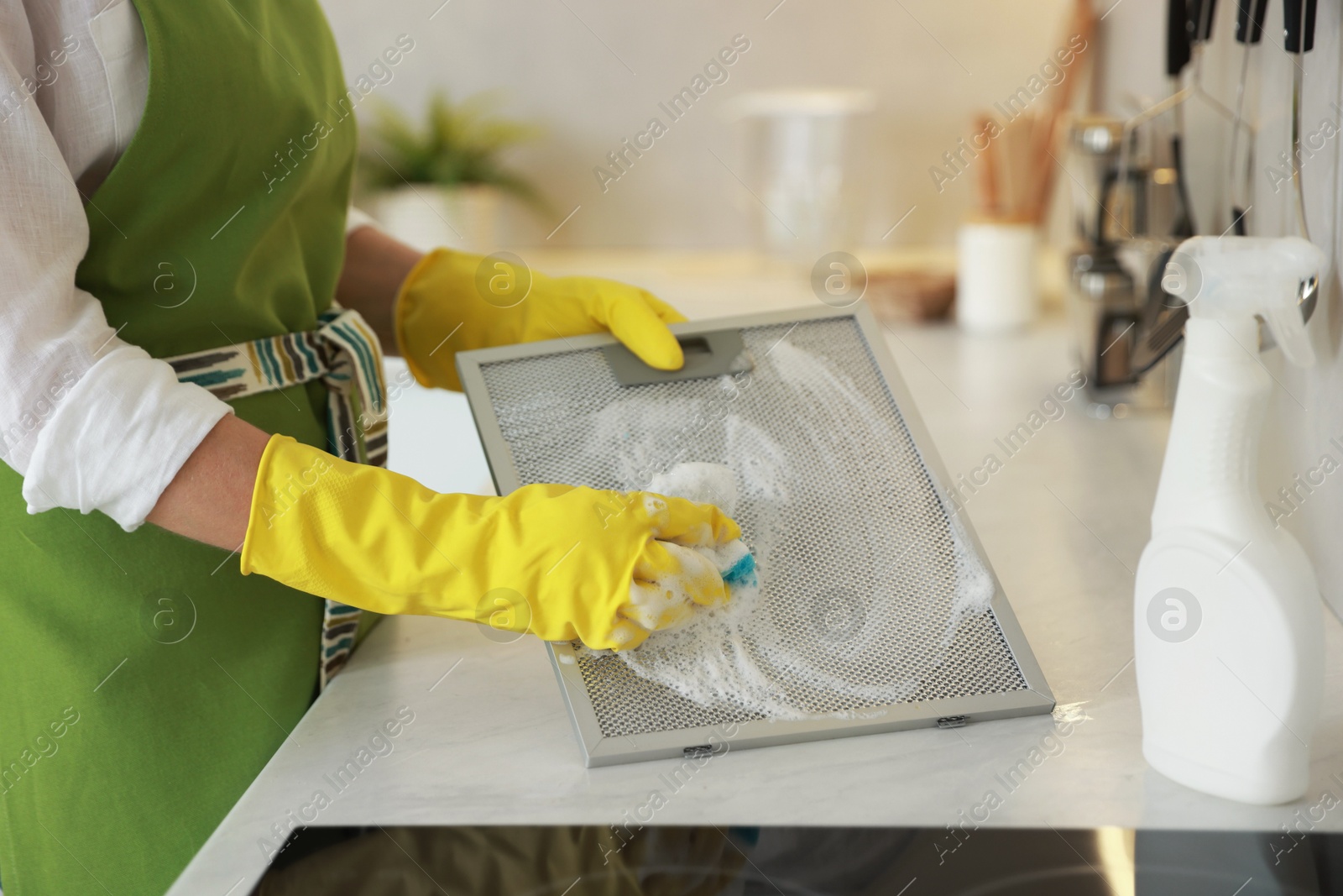 Photo of Woman cleaning filter of kitchen hood with sponge at countertop indoors, closeup